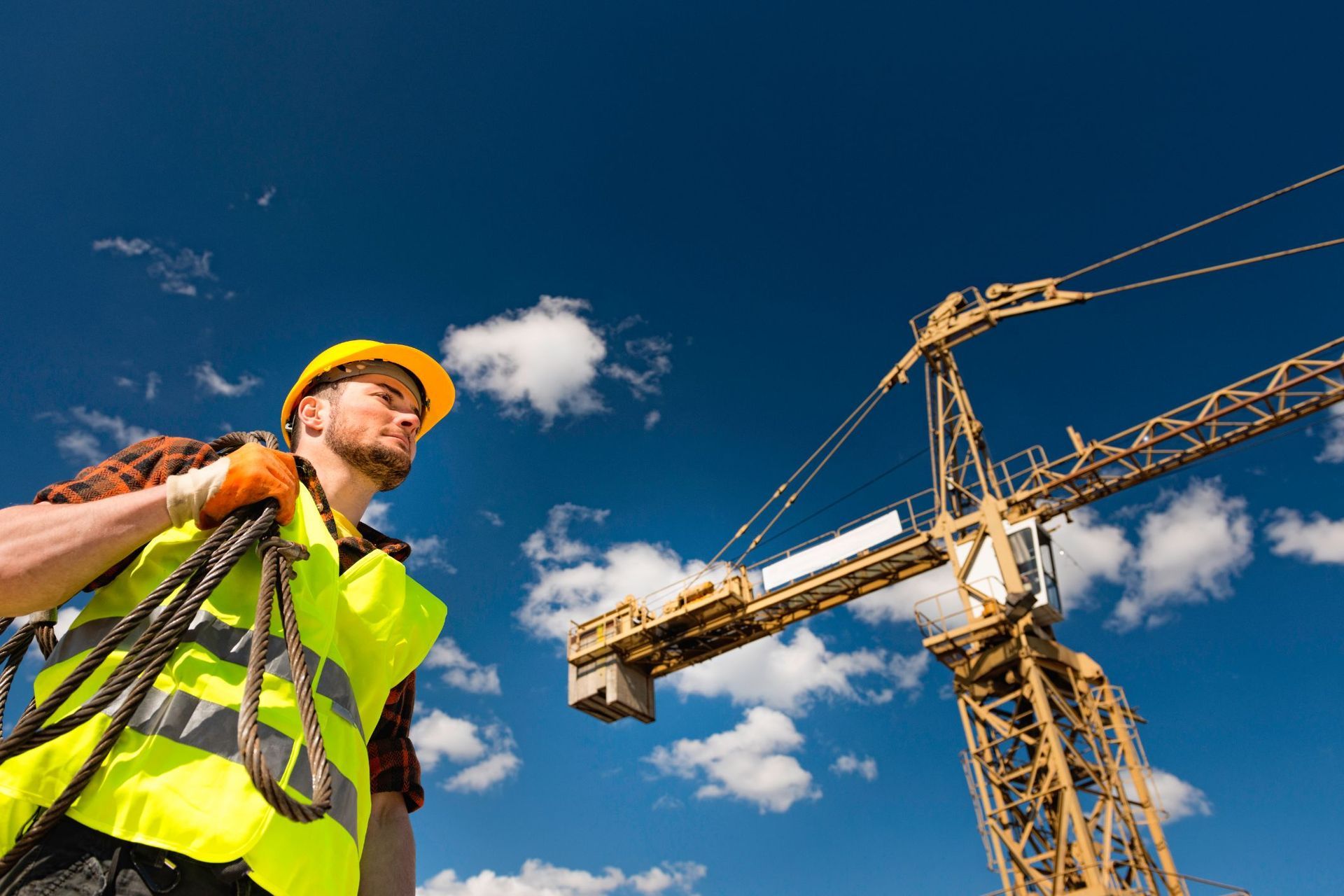 A construction worker is standing in front of a crane on a construction site.