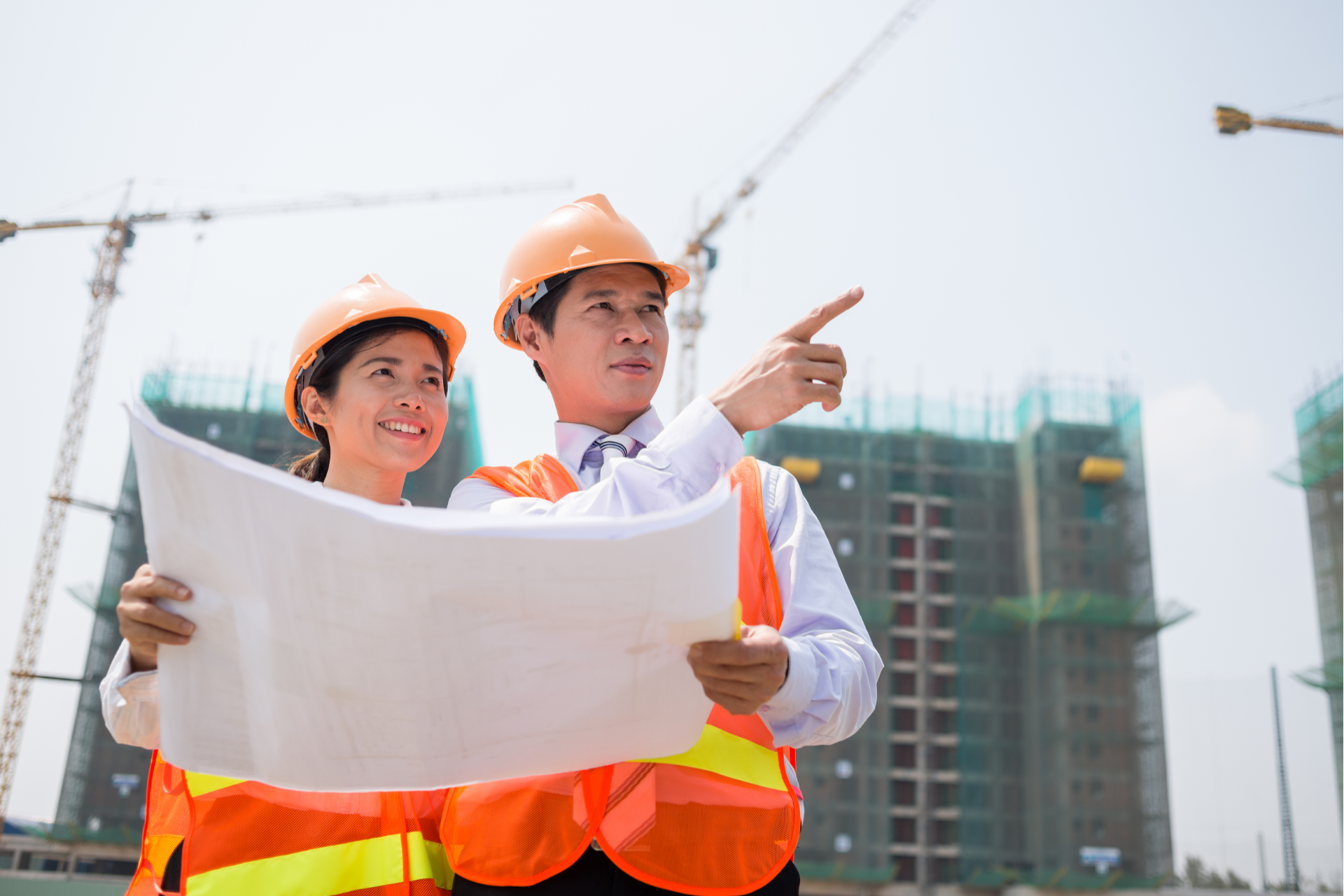 A construction worker is standing in front of a crane on a construction site.