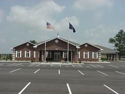 Brick building with US and state flags, parking lot in front.
