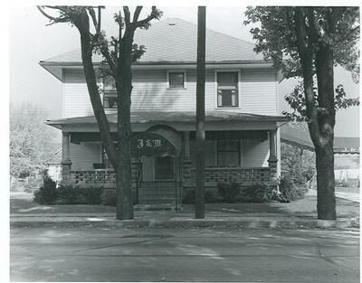 Two-story house with porch, light siding, and trees in front on a street.