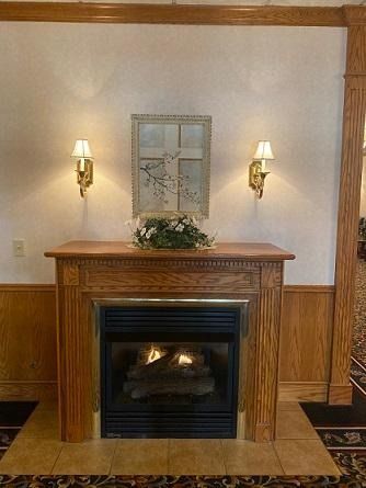 Fireplace with art, sconce lights, floral arrangement. Wooden mantel and paneling.