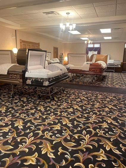 Funeral home interior with several open caskets on display, set on a floral patterned carpet.