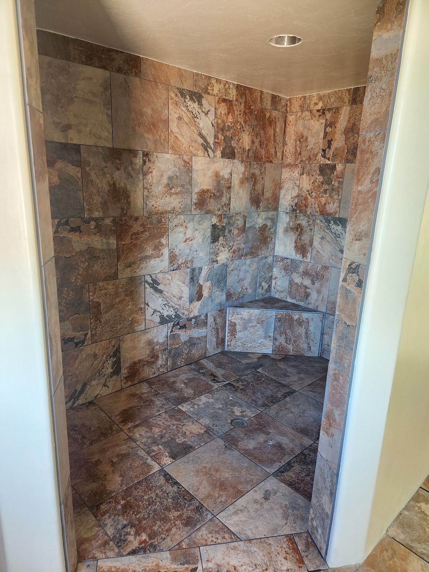 Small tiled shower nook with stone-look walls and floor, viewed through a doorway