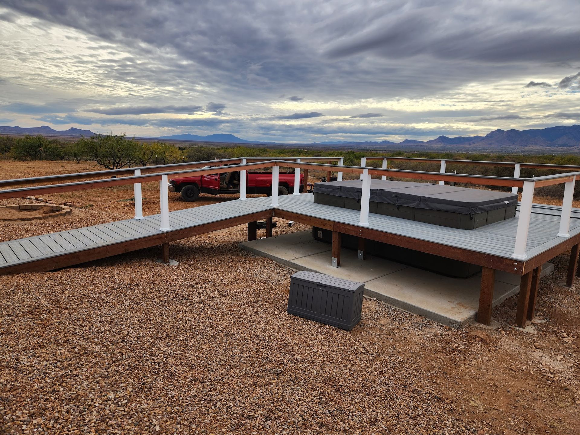 Raised wooden deck overlooking a gravel yard and desert landscape under a cloudy sky