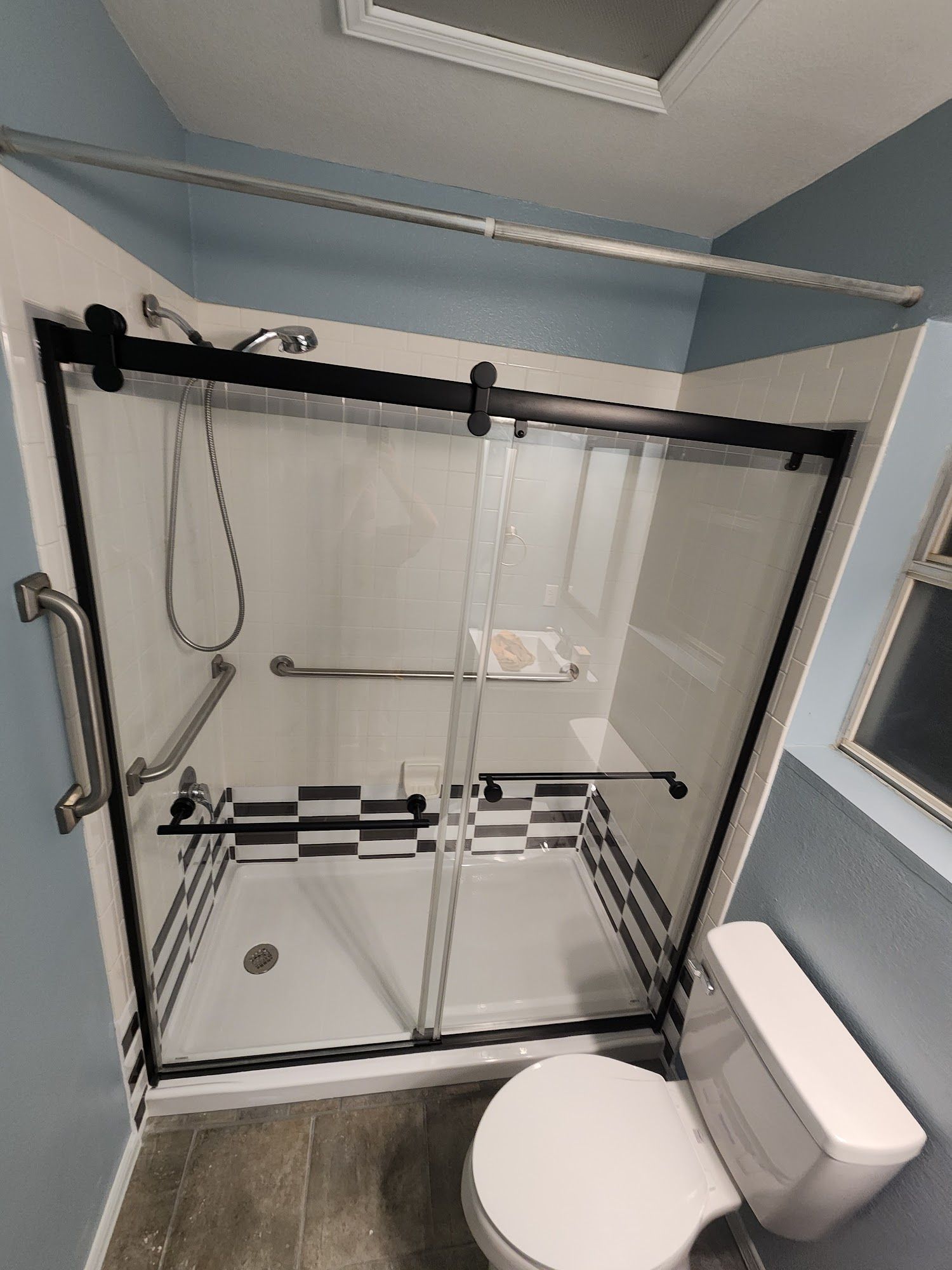Accessible bathroom with a glass walk-in shower and toilet, white and black tile accents, and a shower bench.