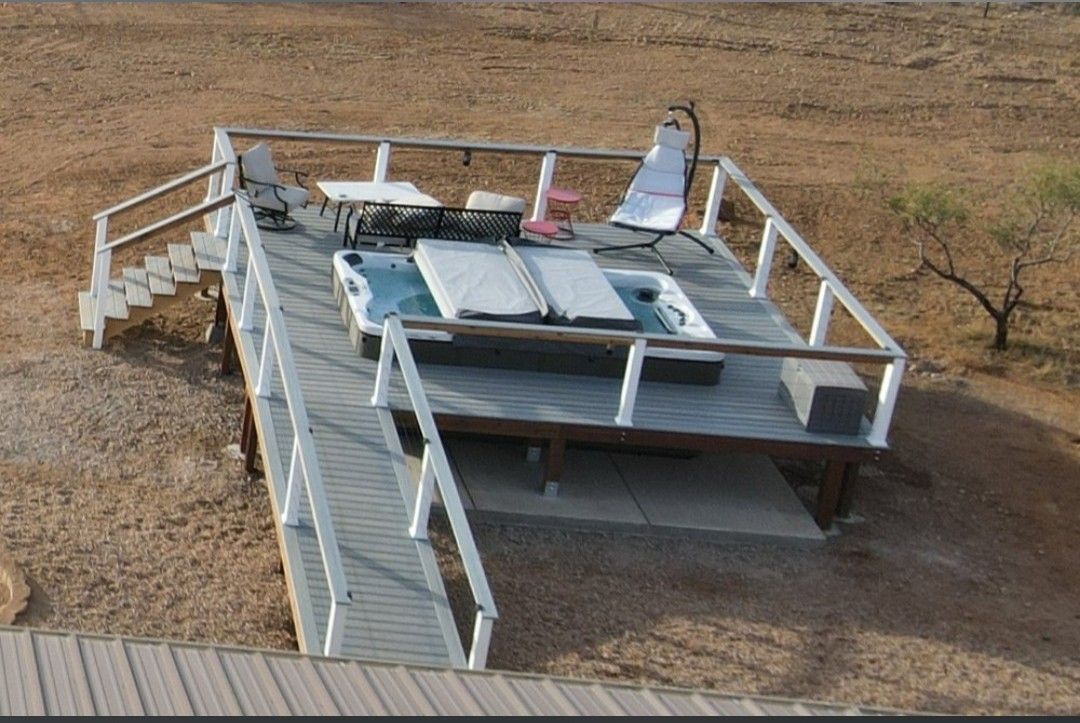 Elevated white platform with railings on a dry, sandy landscape, with stairs and rooftop equipment.