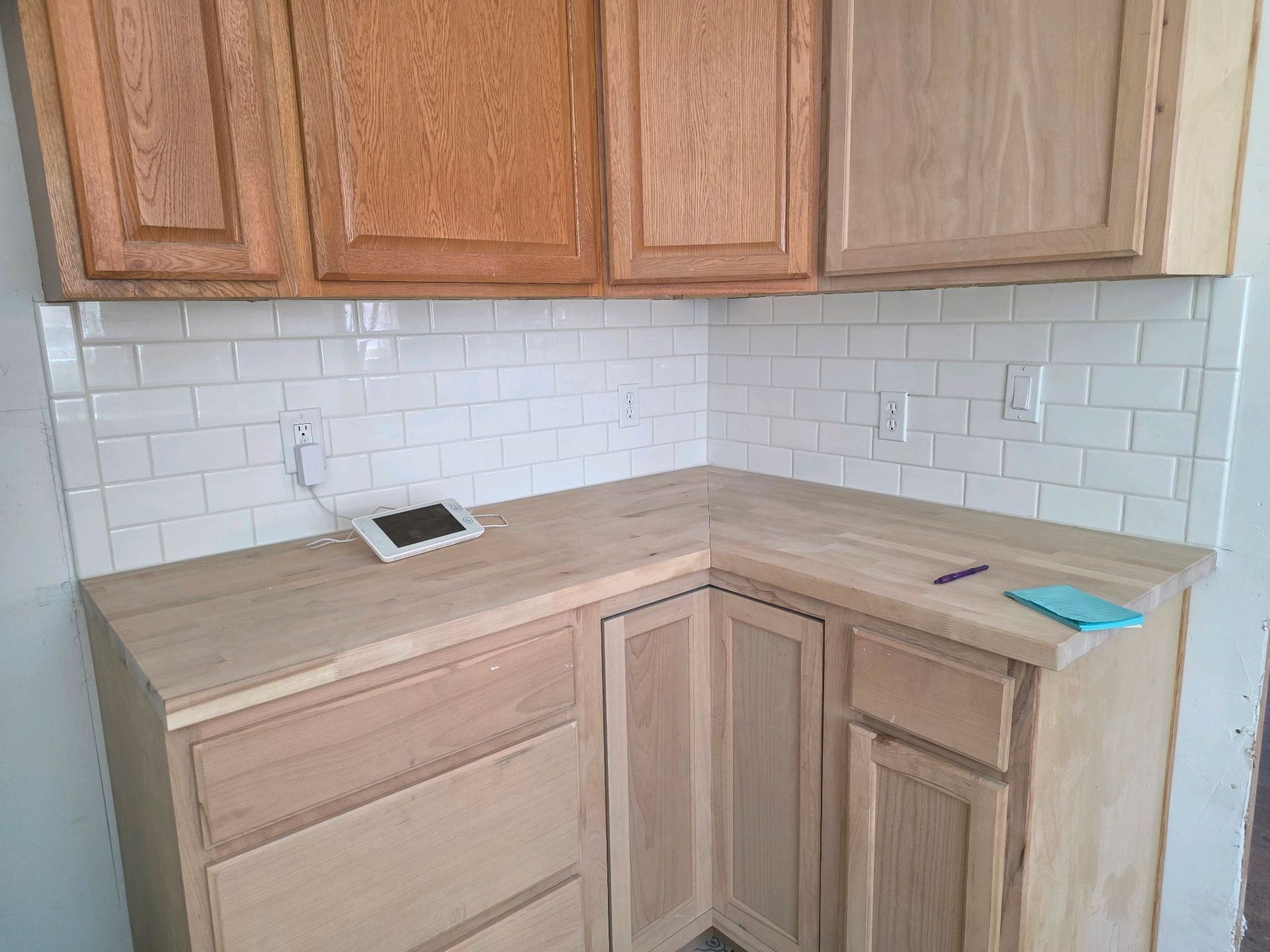 Unfinished kitchen corner with light wood cabinets, beige countertop, white subway tile backsplash