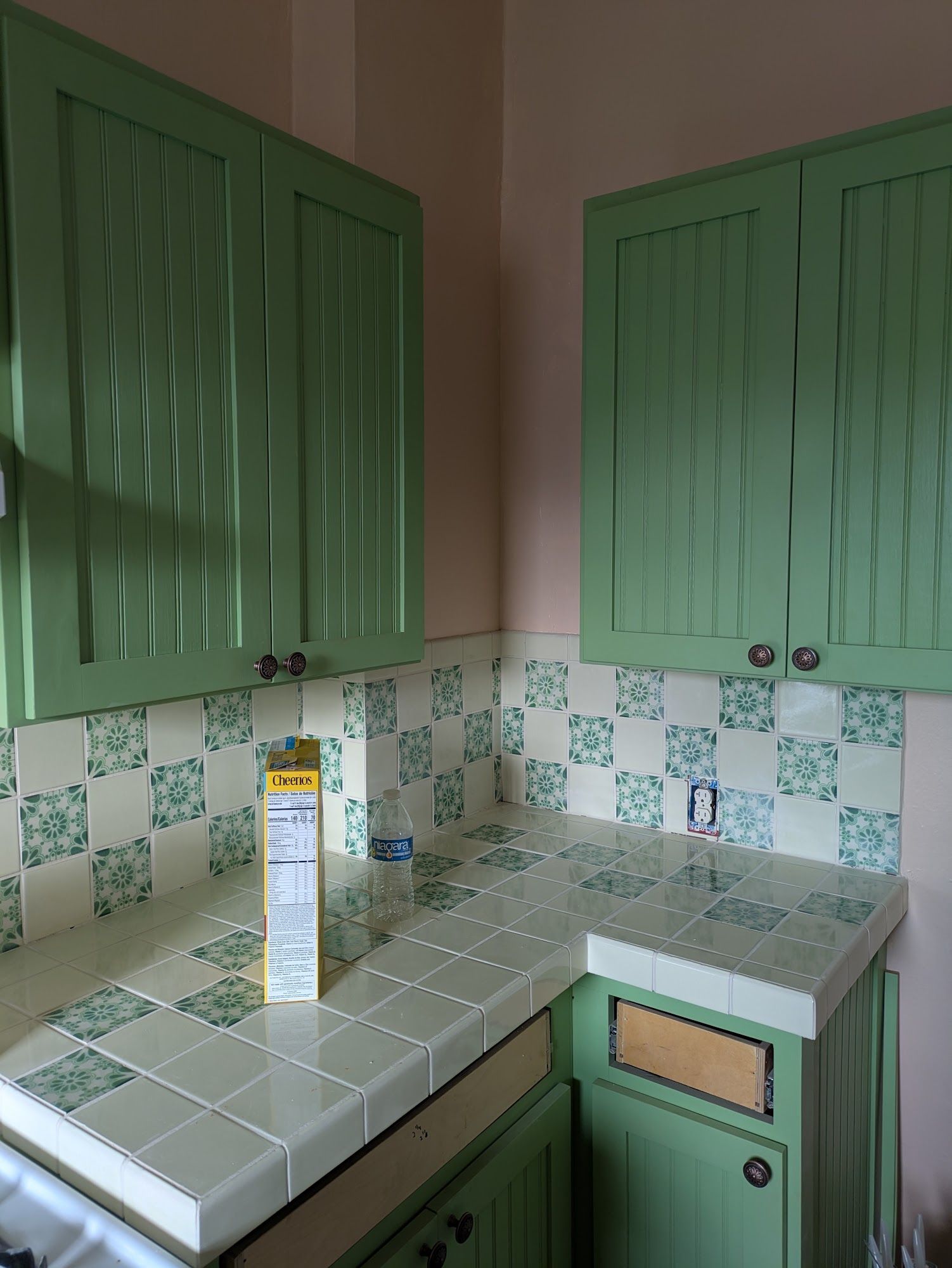 Small kitchen with green cabinets, white tile countertop, and patterned backsplash.