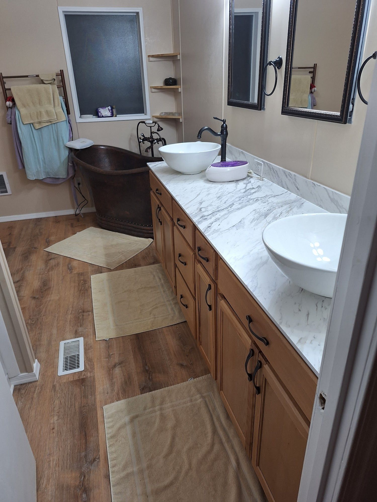 Bathroom with double vanity, large mirrors, brown cabinets, white sinks, and a tub near the window.