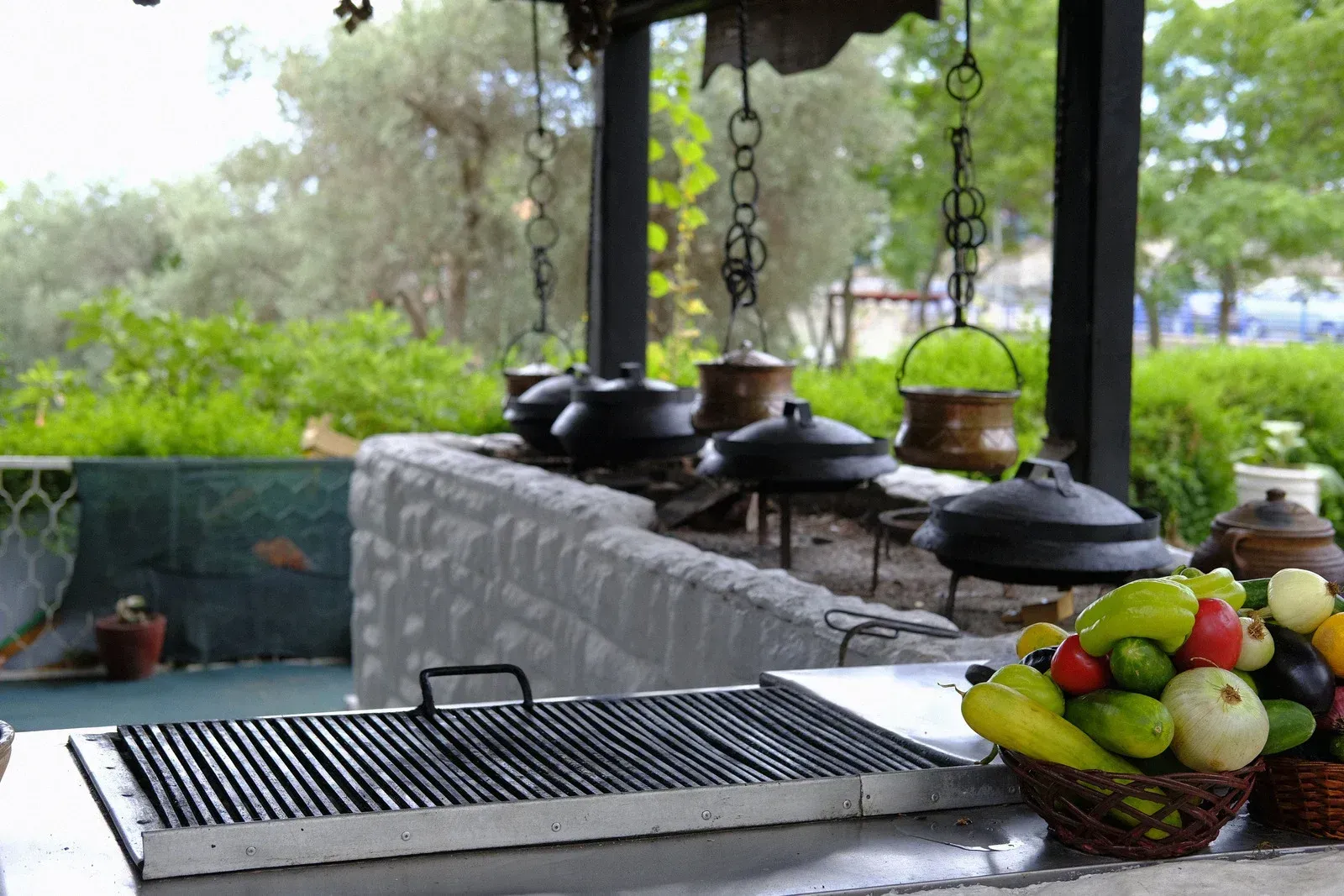 Outdoor buffet table with grill, hanging pots, and bowls of food under a shaded patio