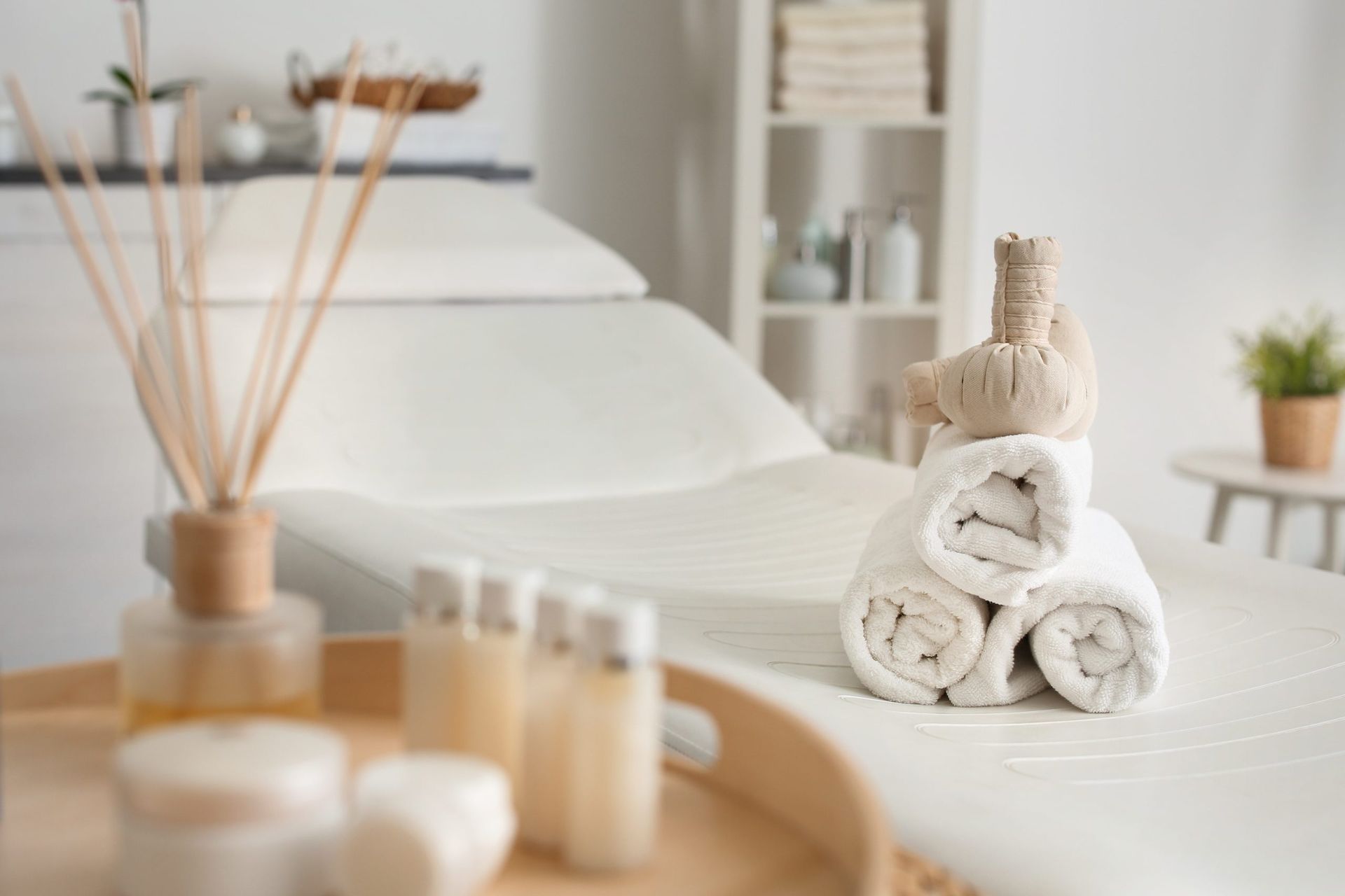 Spa treatment room with rolled white towels on a bed and massage oils in the foreground