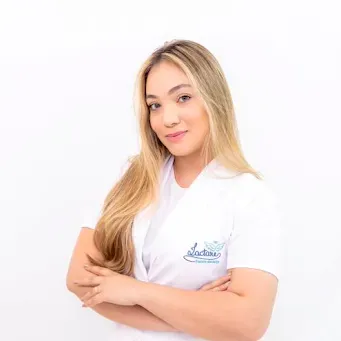 Uma mulher de jaleco branco está de pé com os braços cruzados.