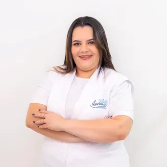 Uma mulher de jaleco branco está de pé com os braços cruzados.