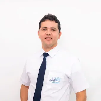 Um homem de camisa branca e gravata azul está parado em frente a uma parede branca.
