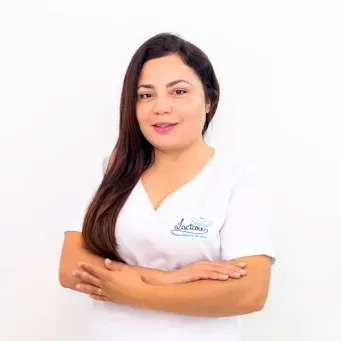 Uma mulher vestindo uma blusa branca está de pé com os braços cruzados.