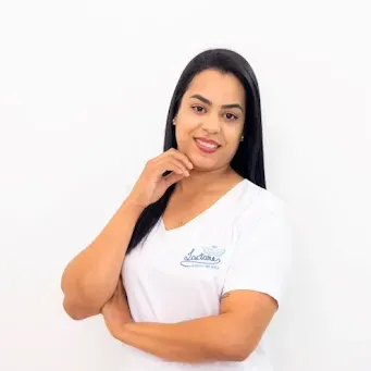 Uma mulher de camiseta branca está de pé com os braços cruzados e sorrindo.