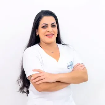 Uma mulher vestindo uma blusa branca está de pé com os braços cruzados e sorrindo.