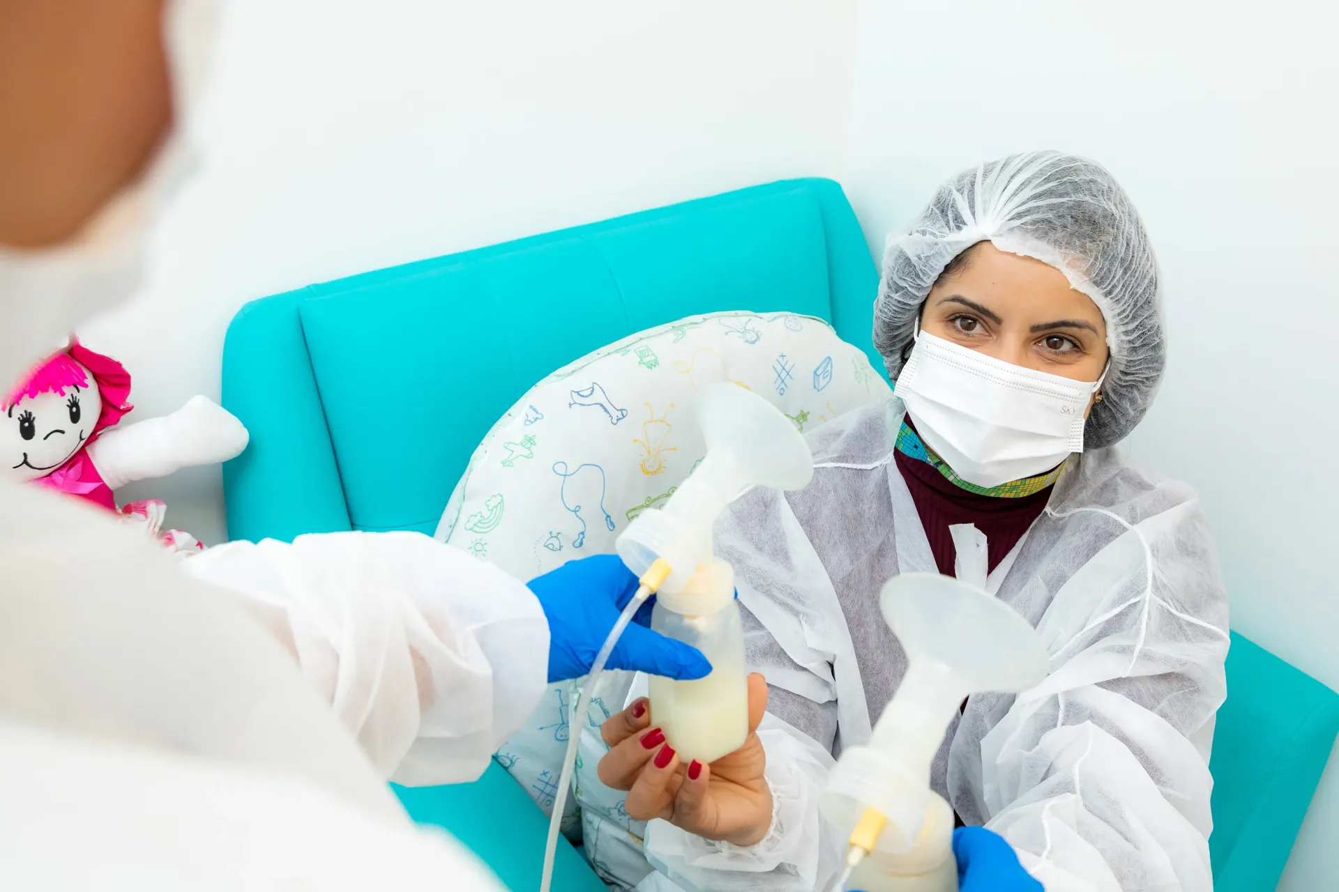 Uma mulher usando máscara e luvas está amamentando um bebê em um hospital.