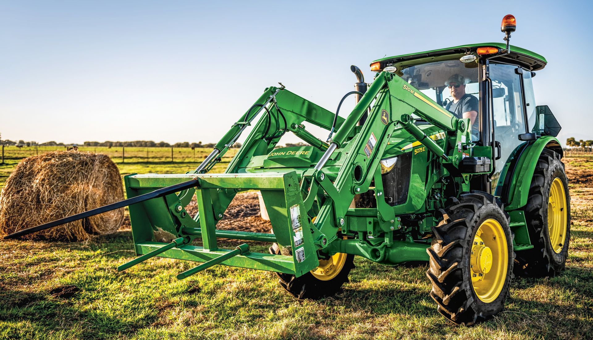 A green and yellow tractor is parked in a dirt field.