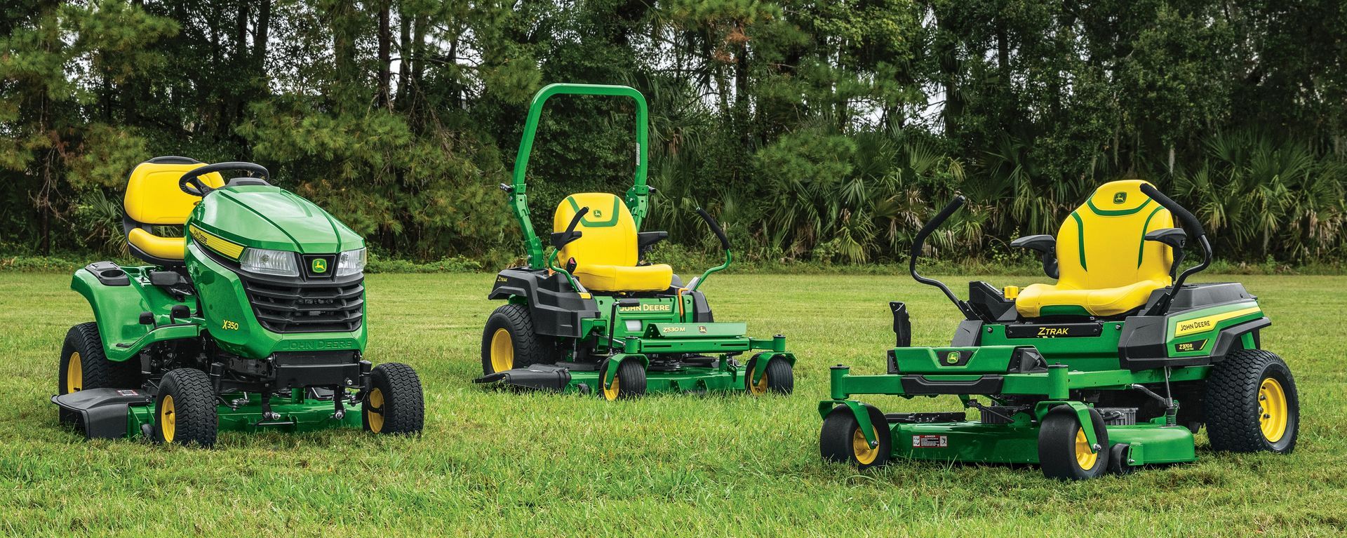 A green and yellow john deere lawn mower is parked in the grass in front of a house.