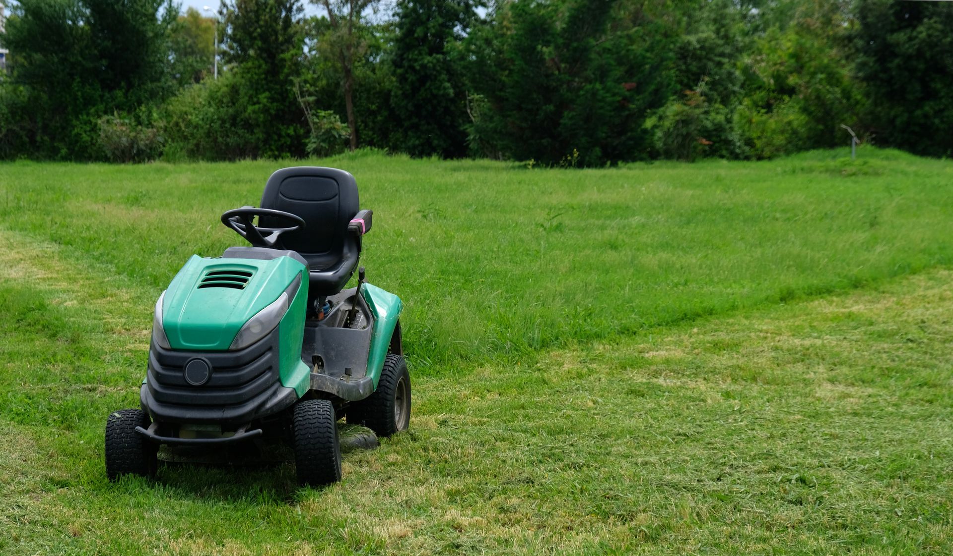 A lawn tractor mowing green grass in a park with visible dirt from recent lawn maintenance work.