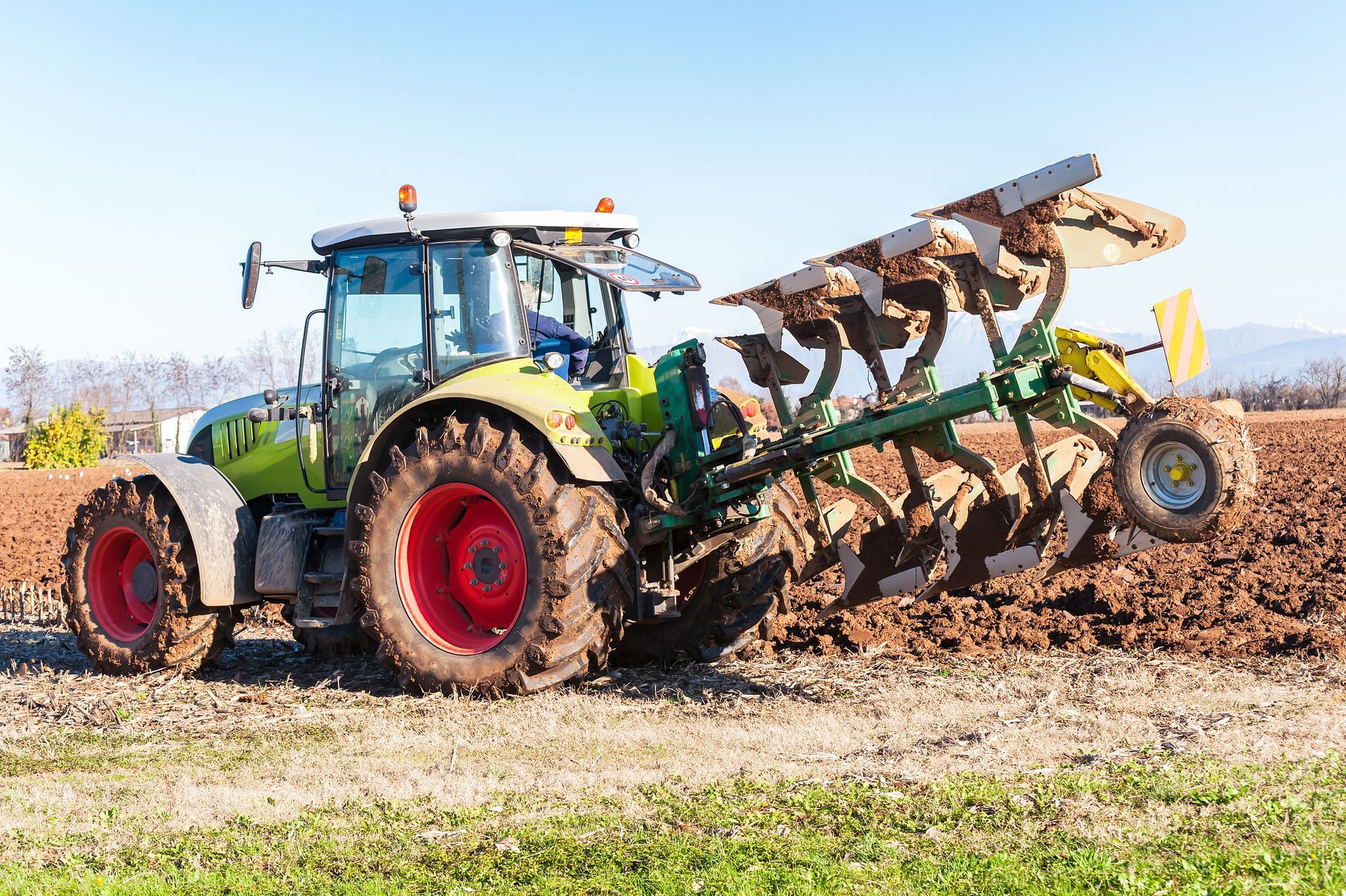 Green tractor plowing a field, a model available at a John Deere Tractor dealer in spring.