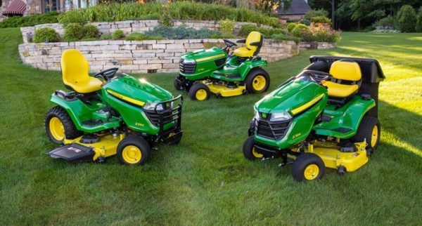 A green and yellow john deere lawn mower is parked in the grass in front of a house.