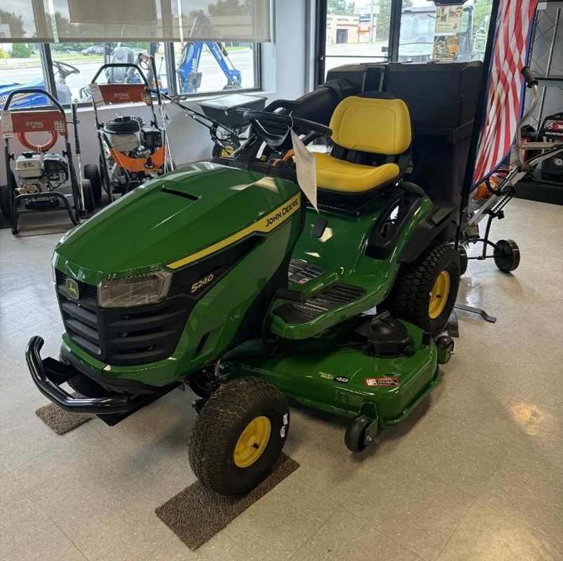 Green John Deere riding lawnmower with yellow seat and wheels in a store setting.