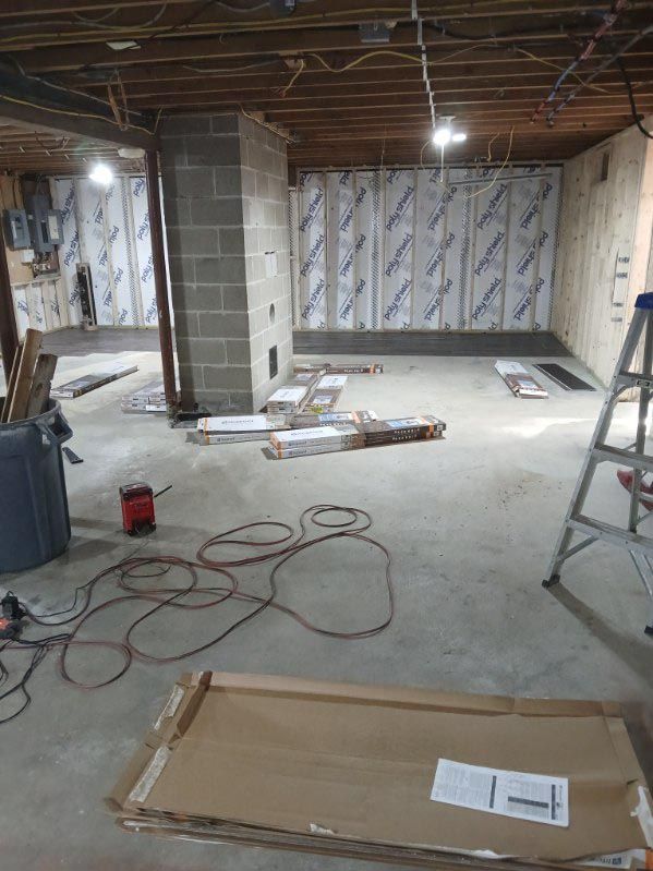 A basement under construction with a ladder and boxes on the floor.