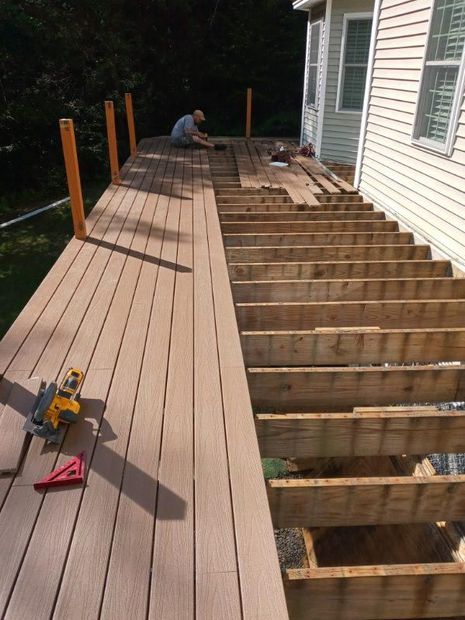 A man is working on a wooden deck in front of a house.