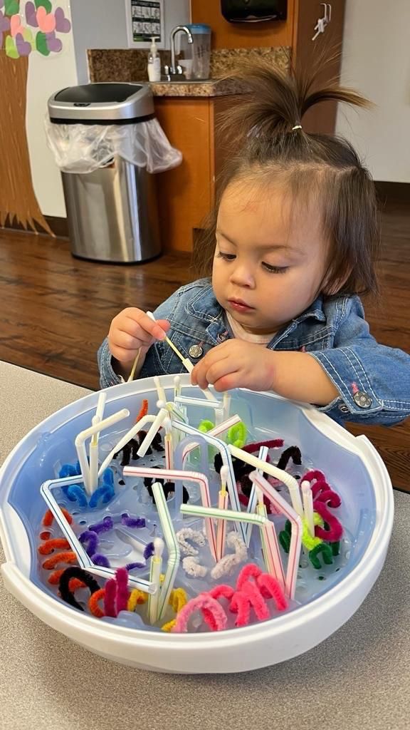 A little girl is playing with pipe cleaners in a bowl.