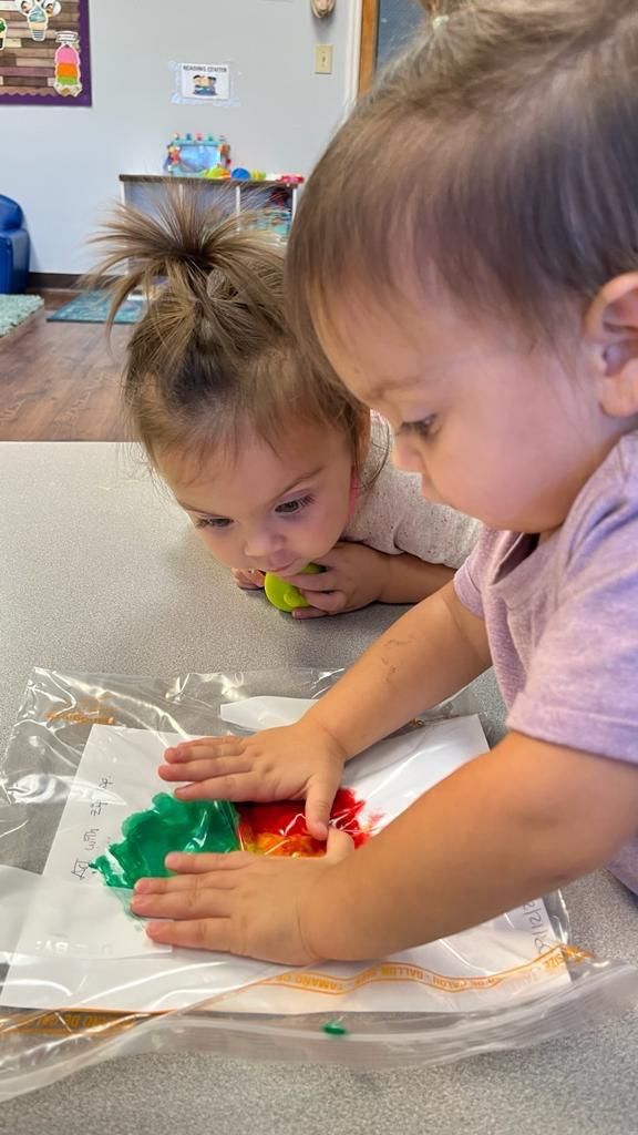 Two toddlers are playing with paint on a piece of paper.