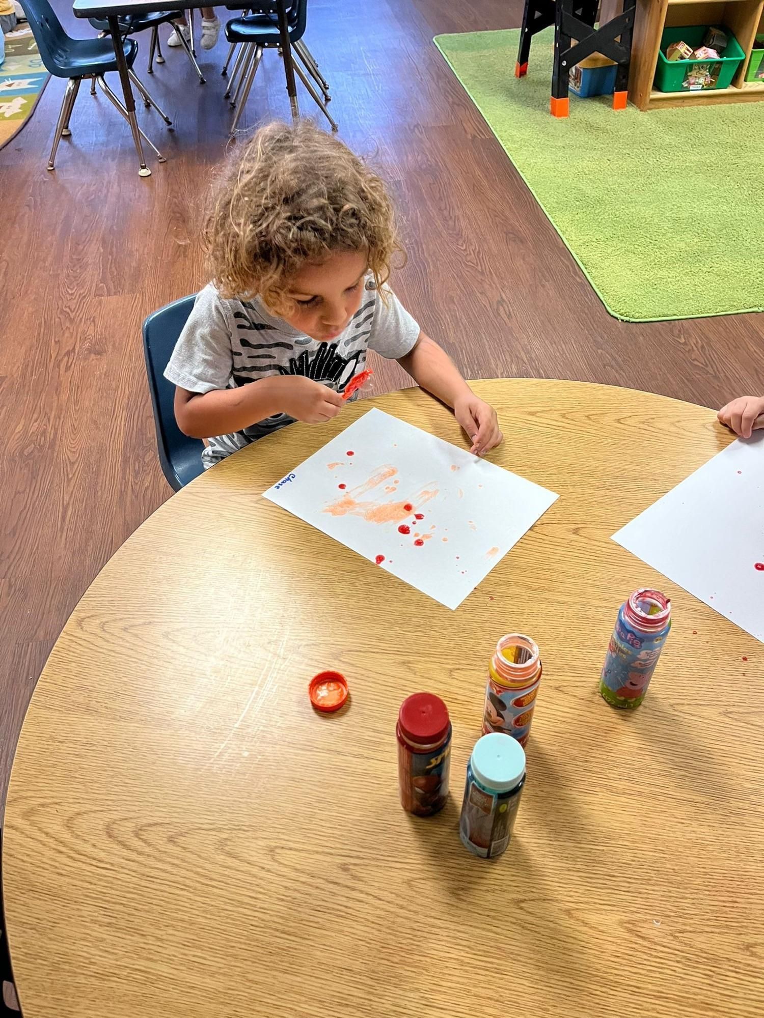 A young boy is sitting at a table painting with a brush.