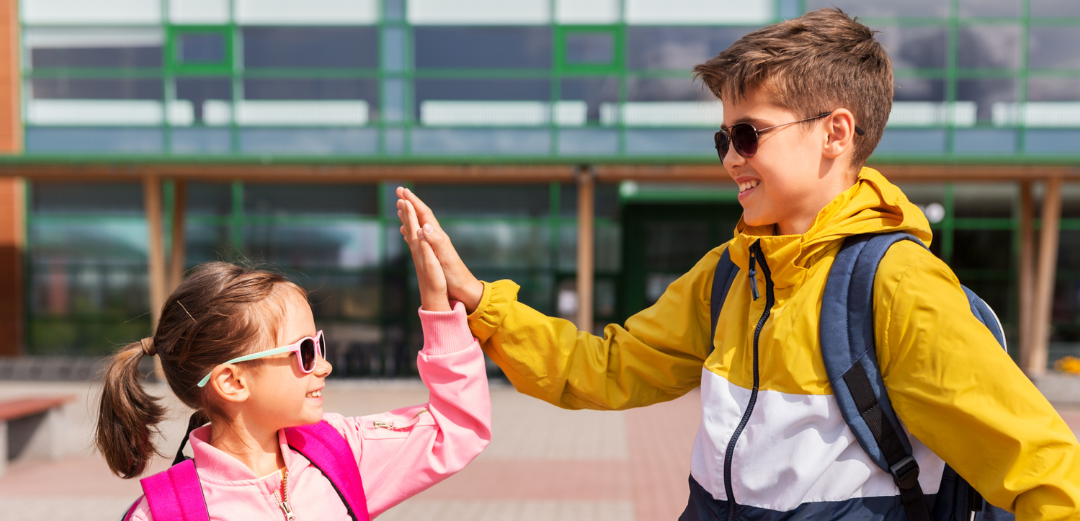 A boy and a girl are giving each other a high five in front of a school building.