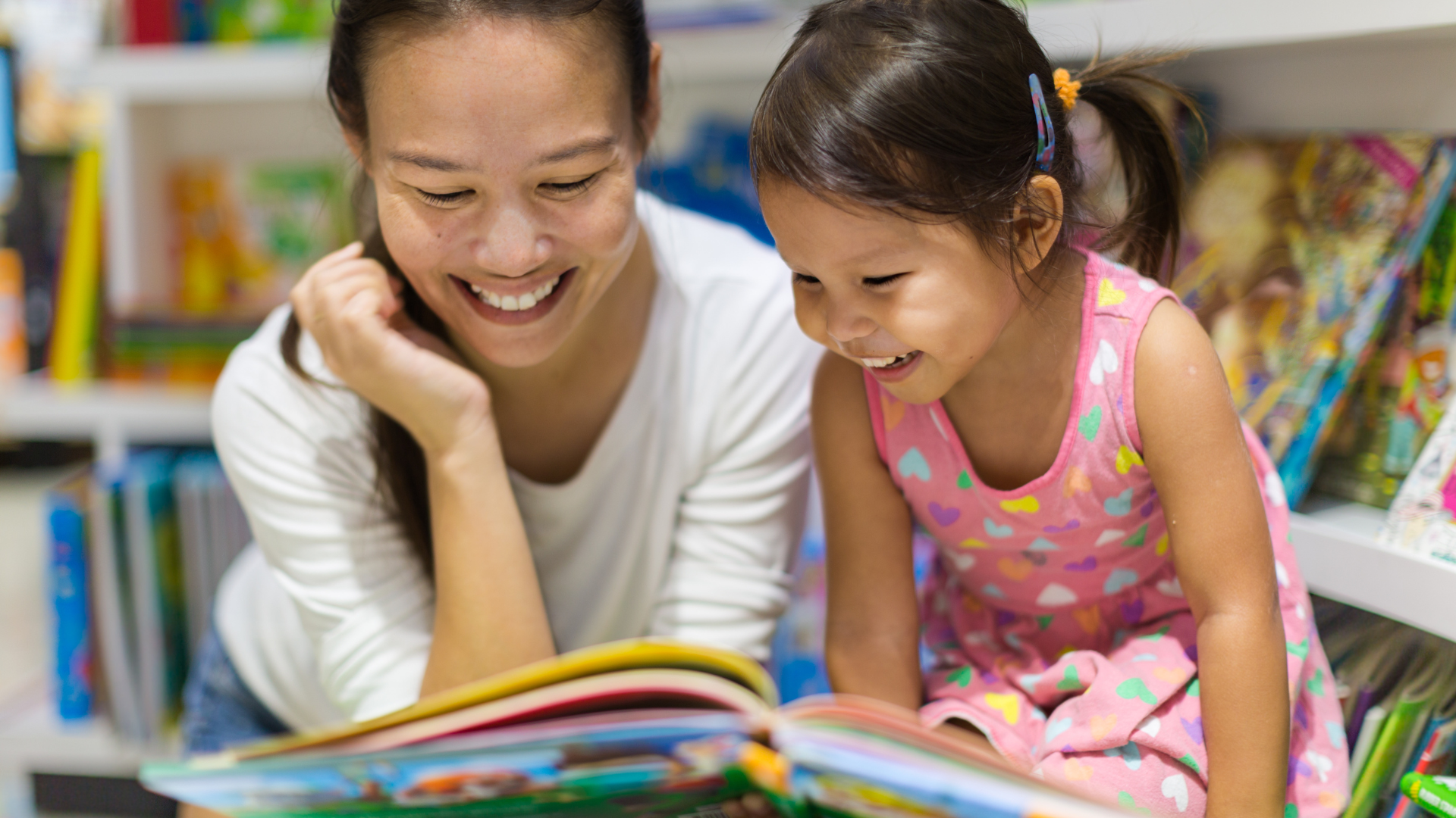 A woman and a little girl are reading a book together in a library.