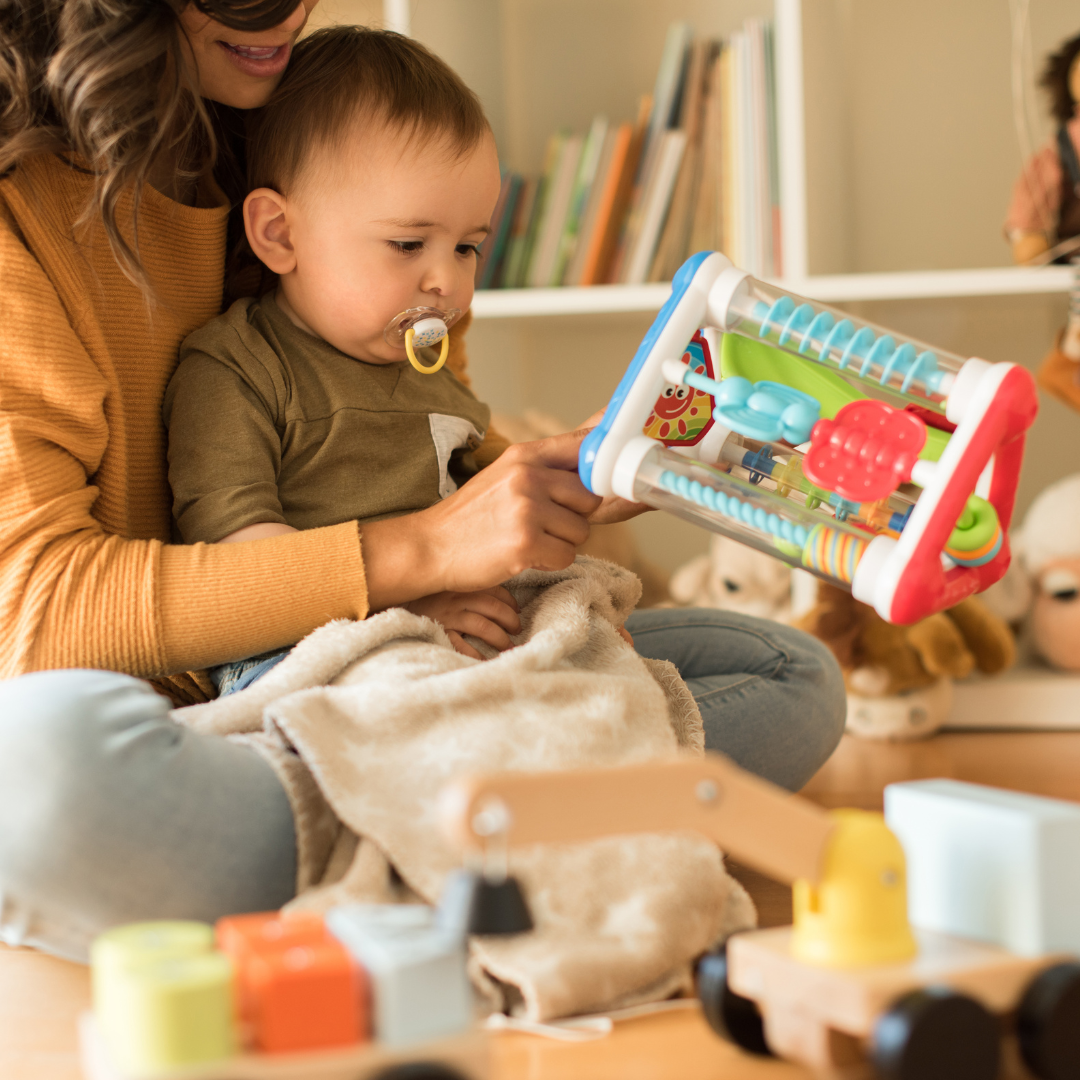 A woman is holding a baby and playing with toys