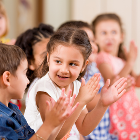 A group of children are clapping their hands together in a classroom.