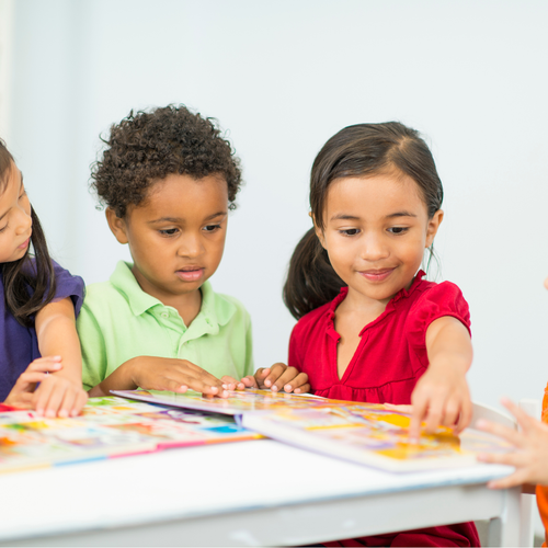 A group of children are sitting at a table looking at a book.