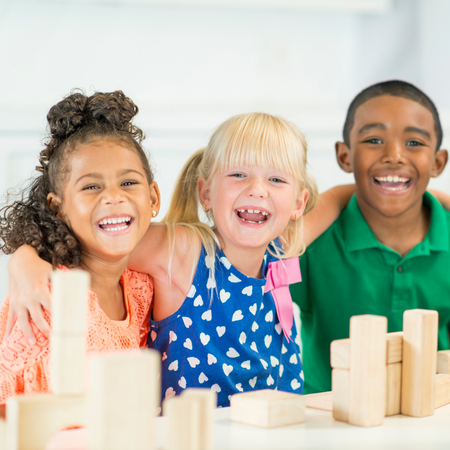 A boy and two girls are sitting at a table with wooden blocks.