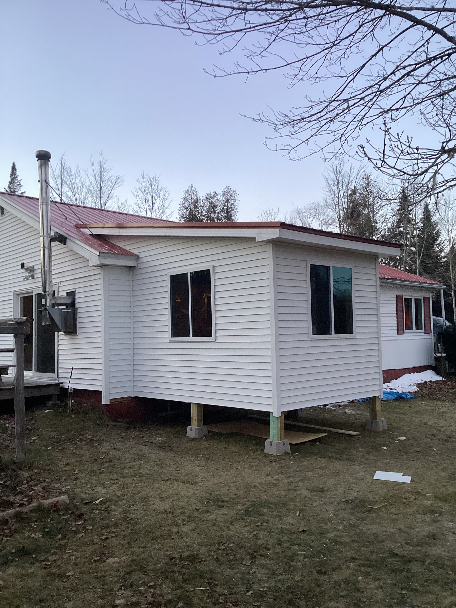 A small white house with a red roof is sitting on stilts in the grass.