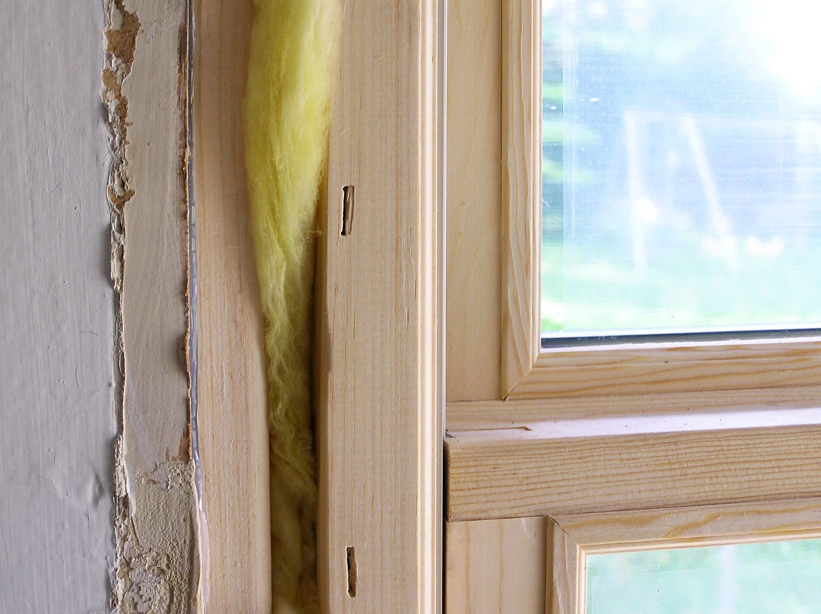 A close up of a wooden window frame with a piece of yellow insulation in the corner.