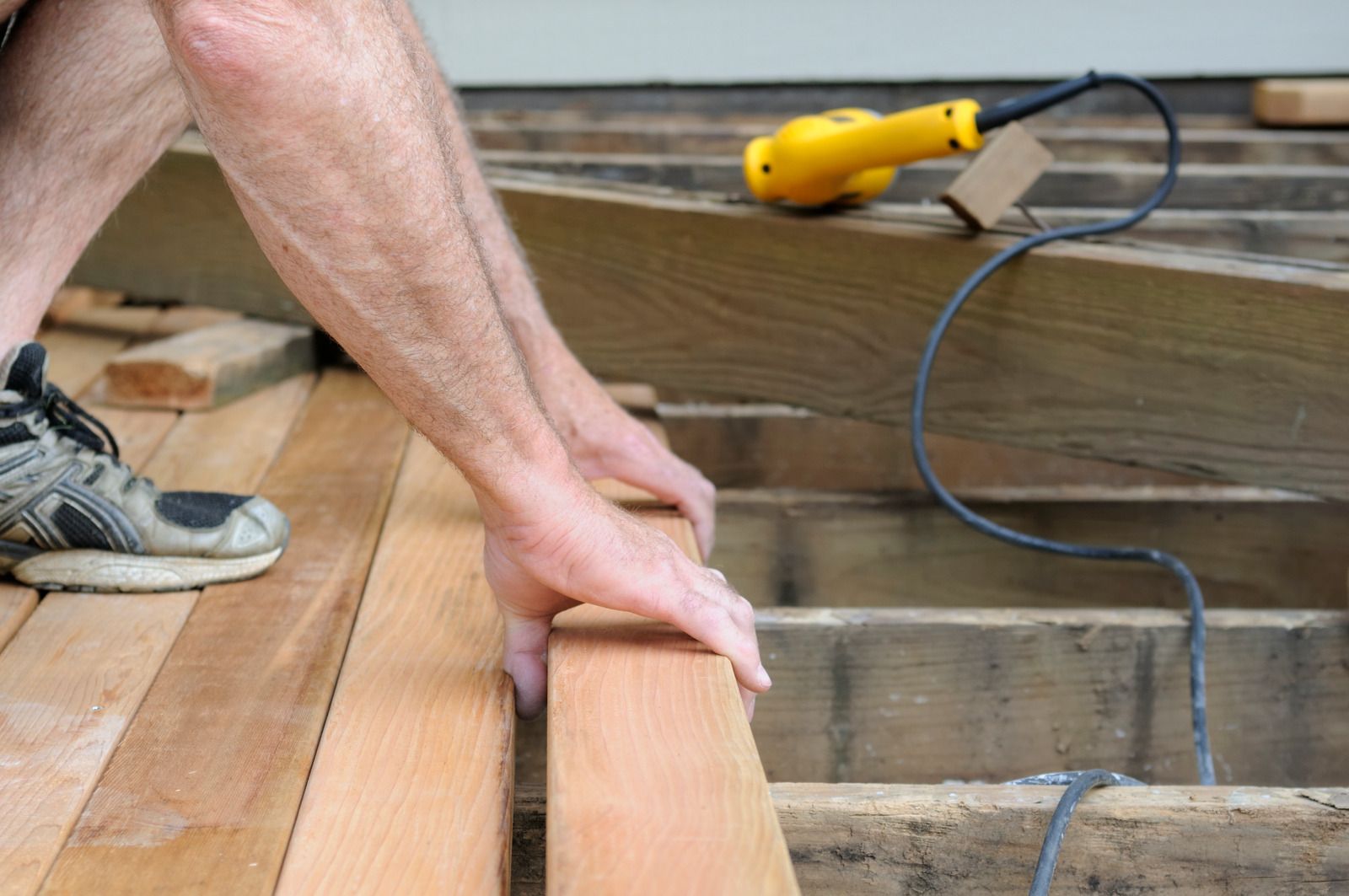 A man is working on a wooden deck with a yellow drill.