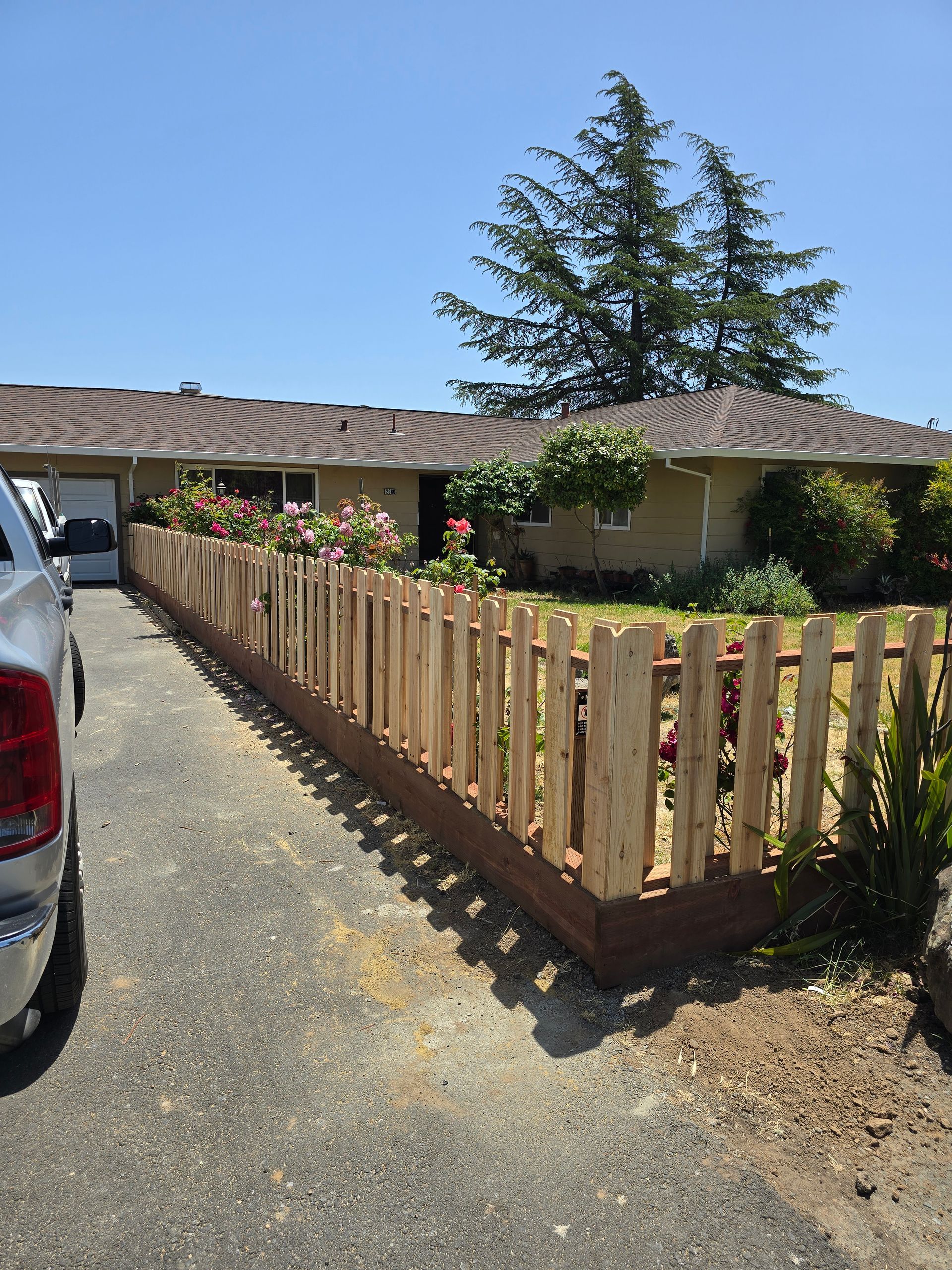 A truck is parked in front of a house with a wooden fence.