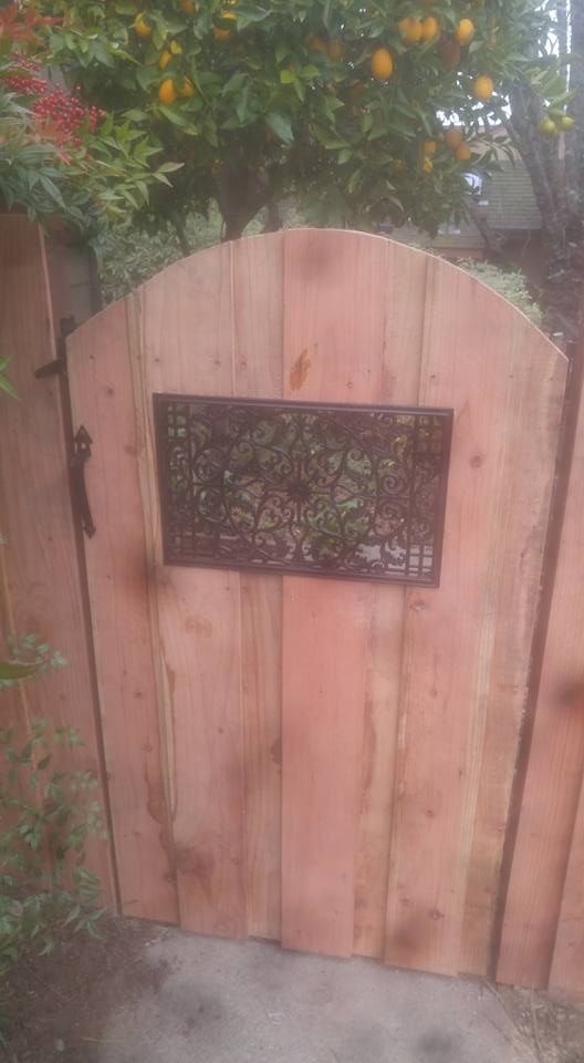A wooden gate with a metal design on it is surrounded by trees.