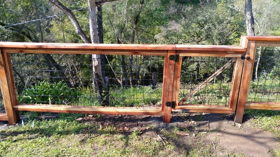 A wooden fence with a gate in the middle of a grassy field.