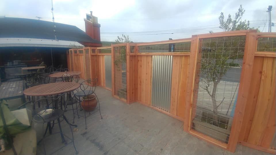 A wooden fence surrounds a patio with tables and chairs.
