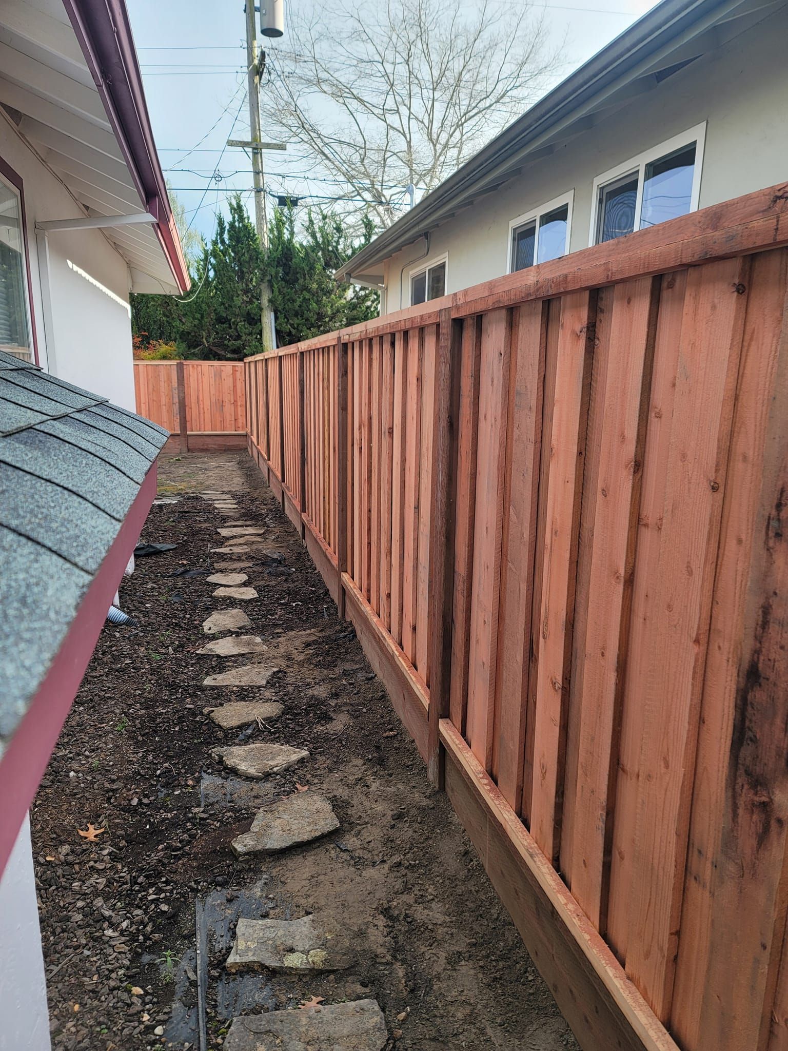 A wooden fence surrounds a dirt path leading to a house.