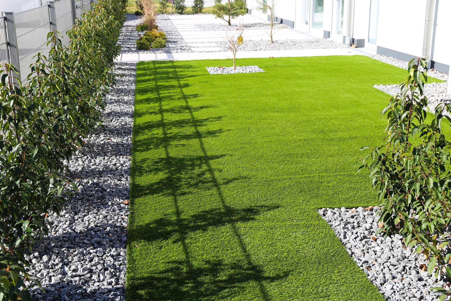 A lush green lawn surrounded by trees and gravel in a backyard