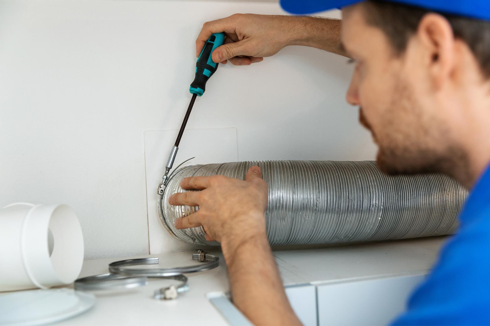 A man is fixing a ventilation pipe with a screwdriver