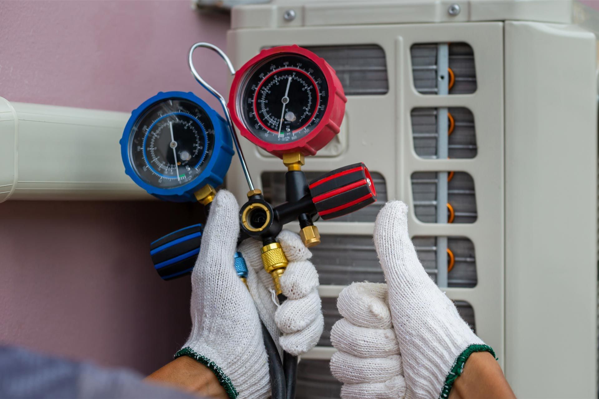 A person is holding two gauges in front of an air conditioner